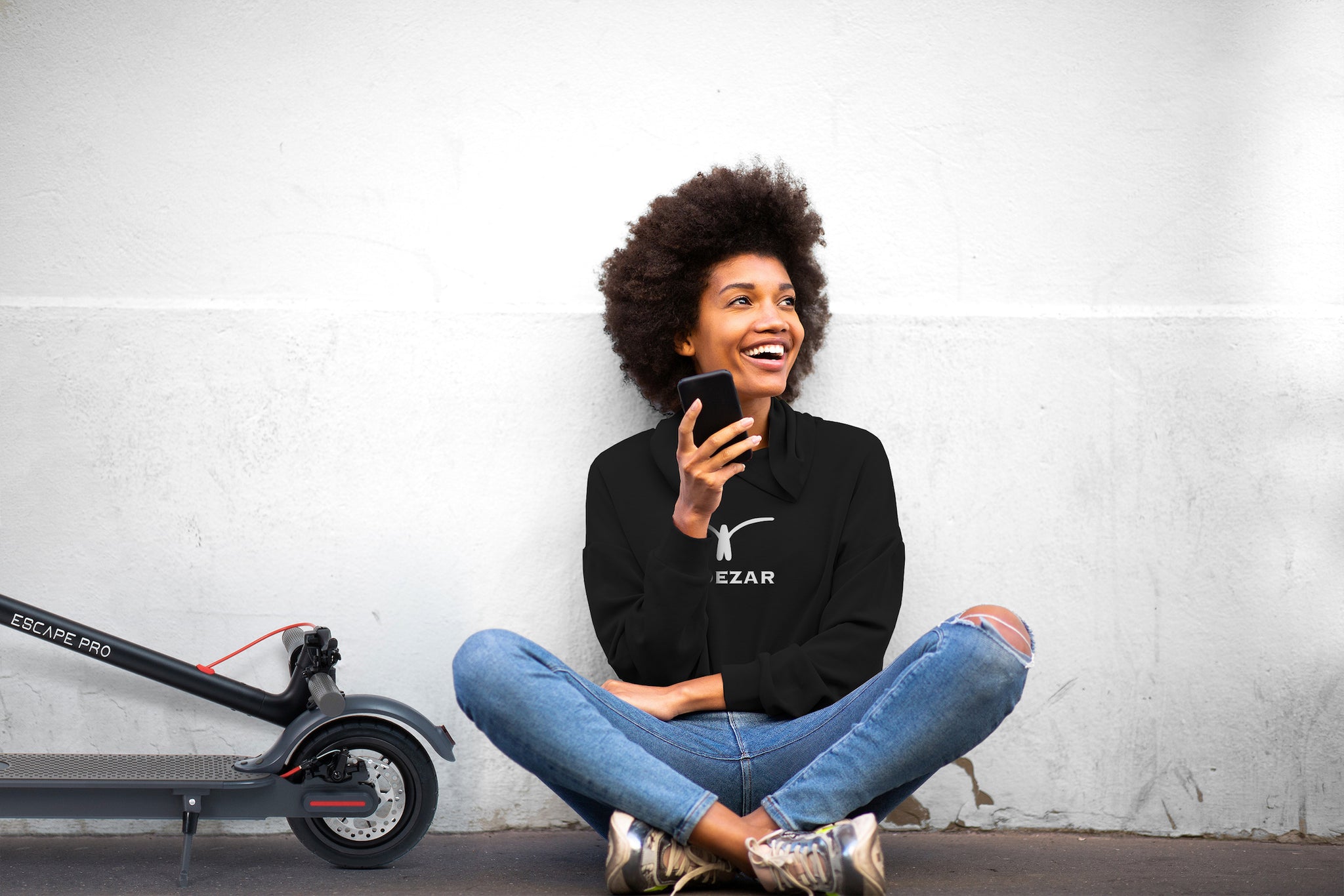 Woman in a black Ridezar jumper, sitting next to an Escape Pro 2 Electric Scooter.